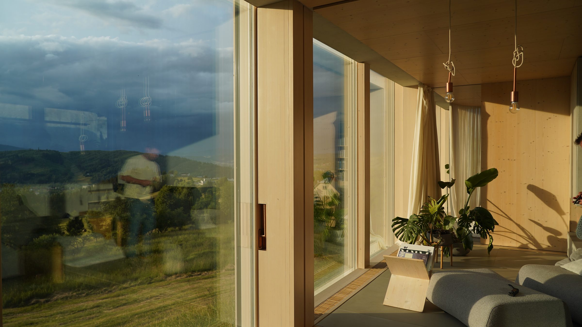 Inside Atelier House: pale timber, copper pendant lamps and a storm sky reflected in the glass