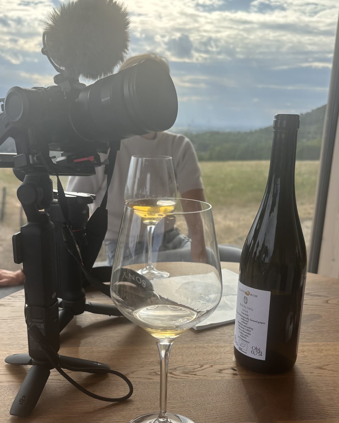 The camera set up on the table by the window, next to a glass of wine